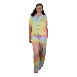 May include: A tie-dye pajama set in pastel colors. The set includes a short-sleeved button-down shirt and matching pants. The shirt has black buttons and a small logo near the hem. The pants have an elastic waistband.