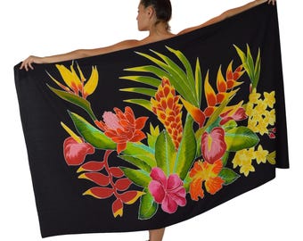 May include: Black sarong featuring a vibrant floral design. The artwork includes colorful tropical flowers and green leaves in shades of red, orange, yellow, and pink. The sarong is held open, showcasing the full design.