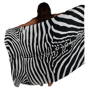 May include: A black and white zebra print sarong, a type of wrap skirt, is draped over a person's shoulders. The sarong is made of a lightweight fabric and has a flowing design.