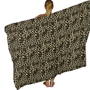 May include: A large, rectangular leopard print scarf or wrap. The fabric features a tan background with dark brown and black spots. The scarf is held up, displaying the full pattern and texture of the material.