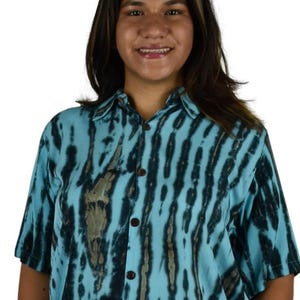 May include: A short-sleeved shirt with a blue and black tie-dye pattern. The shirt has a collared neckline and brown buttons. The fabric has a vertical stripe design. The shirt is worn by a person.