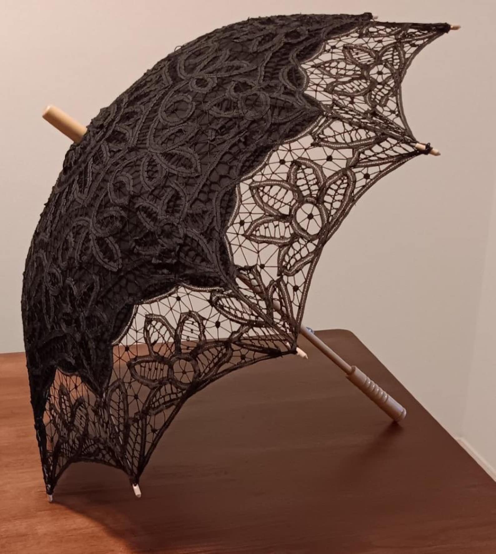 Side view of black lace parasol with floral embroidery, scalloped edges, and a carved wooden handle for vintage gothic flair