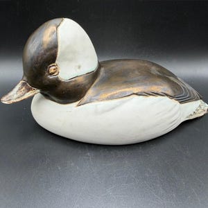 Puede incluir: Figura de pato de cerámica con cuerpo blanco y cabeza y espalda marrón oscuro. La cabeza del pato tiene una mancha blanca y el pico es de color marrón claro. El objeto es decorativo.