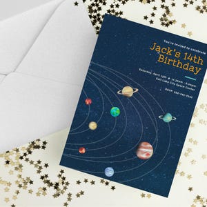 May include: A navy blue birthday invitation with a solar system design. The invitation reads "Jack's 14th Birthday" with event details. An open white envelope is visible, along with star-shaped confetti.
