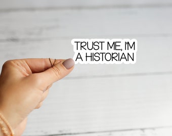 Op de afbeelding: Witte sticker met zwarte tekst die "TRUST ME, I'M A HISTORIAN" zegt.