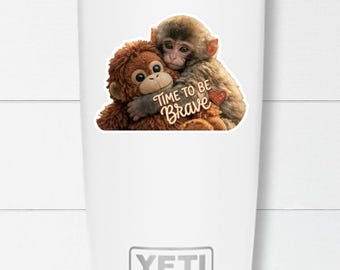 Op de afbeelding: Witte Yeti-beker met een afbeelding van twee knuffelende apen. De apen zijn bruin en bruin, met de tekst "TIME TO BE BRAVE" en een rood hart. De beker heeft een zilveren rand en het Yeti-logo.