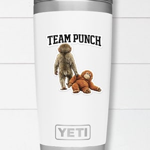 May include: White insulated tumbler with a silver rim and base. The tumbler features a sticker with the text "TEAM PUNCH" above illustrations of two orangutans. The brand name "YETI" is printed at the bottom.