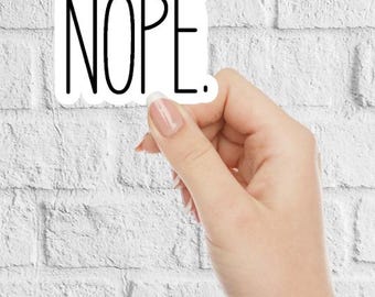 May include: A white sticker with black text that reads "NOPE." The sticker is being held by a hand against a white brick wall.