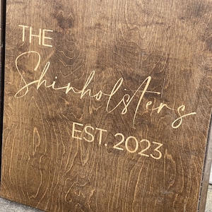 May include: A brown wooden sign with the text "THE Shinholsters EST. 2023" in gold lettering.