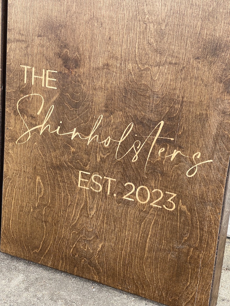 May include: A brown wooden sign with the text "THE Shinholsters EST. 2023" in gold lettering.