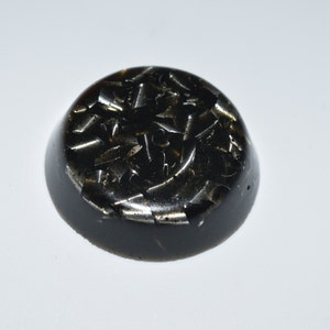 May include: A round, black, resin-based, crystal healing orgonite with embedded metallic flakes.