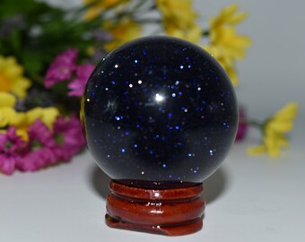 May include: A dark blue, sparkly crystal ball on a wooden stand. The ball is filled with tiny, glittering particles that resemble stars.