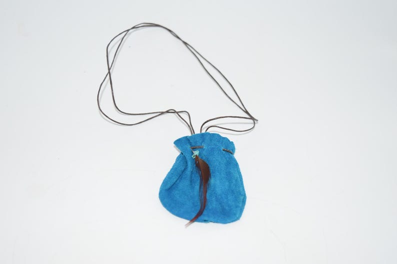 K&ouml;nnte beinhalten: Ein kleiner blauer Beutel aus Wildleder mit einer braunen Feder, die daran h&auml;ngt. Der Beutel ist an einer braunen Schnur befestigt.