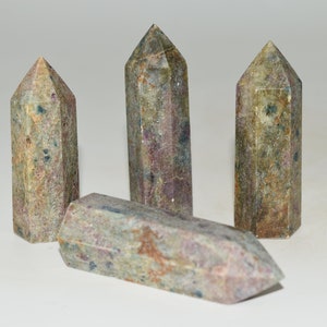 May include: Four natural stone obelisks with a mix of colors including green, pink, and brown. Three are upright, and one is lying down. The obelisks have a faceted design and are likely used for decorative or spiritual purposes.