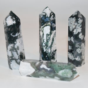 Puede incluir: Cuatro puntas de cristal de ágata musgosa verde, blanca y negra. Las puntas están dispuestas en fila, con las dos de los extremos apuntando hacia arriba y las dos del medio apuntando hacia abajo.