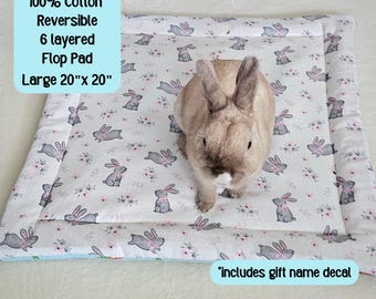 May include: A reversible, 100% cotton, 6-layered flop pad, 20" x 20", with a bunny and floral pattern. The pad has a light blue border and includes a gift name decal. A small rabbit sits on the pad.