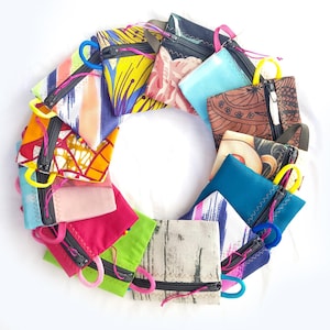 Op de afbeelding: Een verzameling kleurrijke, kleine etuis met ritssluiting, gerangschikt in een cirkelvormig patroon. De etuis hebben verschillende patronen en kleuren, waaronder roze, blauw, geel en bedrukte stoffen. Elke etui heeft een contrasterende rits en een lus.