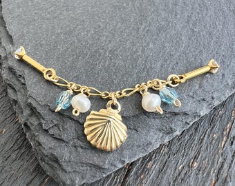 May include: Gold-toned necklace with a seashell pendant, pearls, and blue crystal accents. The necklace features a delicate chain and is designed with a nautical theme. The seashell pendant is detailed and adds a touch of elegance.