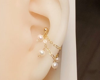 May include: A gold-colored ear cuff featuring a small ball stud and dangling chains. The chains are adorned with small, white pearls. The earring is designed to be worn on the upper ear cartilage.