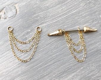 May include: Gold body jewelry with a chain dangle. The jewelry is a barbell with two gold wings on the ends. The chain dangle is made of four gold chains.