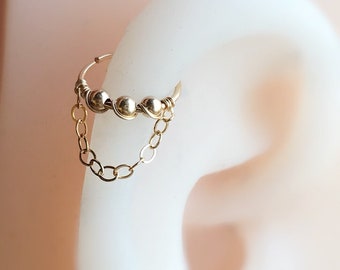 May include: Gold hoop earring with a dangling chain and three small gold beads.
