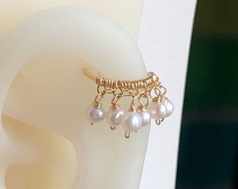 Puede incluir: Un aro de oreja de oro con una fila de pequeñas perlas blancas que cuelgan.