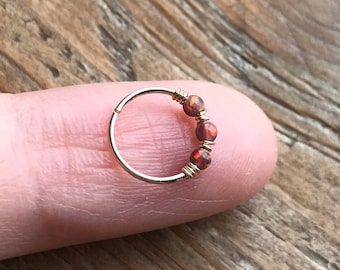 May include: Gold hoop nose ring with three small, iridescent opal beads.
