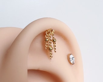 May include: Gold chain dangle earring with small gold beads. The earring is worn in a helix piercing.