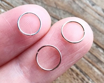 May include: Three silver nose rings, each with a different diameter, are displayed on a finger.
