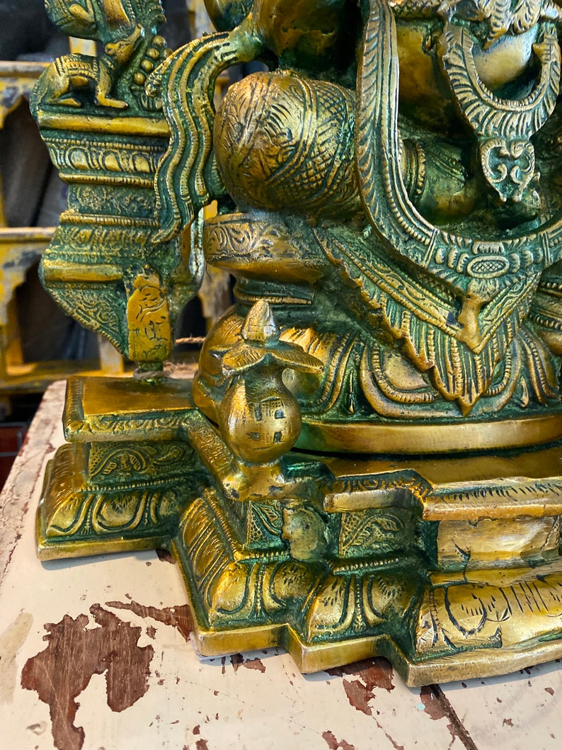 May include: A gold-colored metal statue of a deity with intricate details and a green patina. The statue is sitting on a base with ornate carvings.