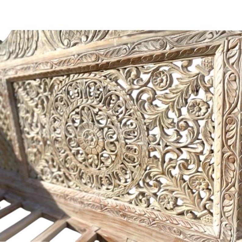 May include: A whitewashed wooden headboard with intricate carved floral designs. The headboard features a large, circular design in the center, surrounded by smaller floral motifs.
