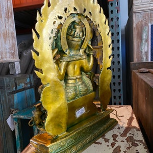 May include: A gold-colored metal statue of a deity with a halo of flames. The statue is sitting on a green and gold base. The statue is about 12 inches tall.