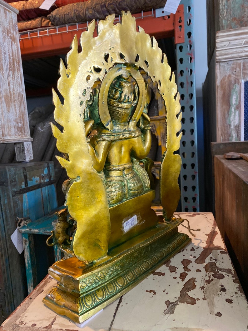 May include: A gold-colored metal statue of a deity with a halo of flames. The statue is sitting on a green and gold base. The statue is about 12 inches tall.