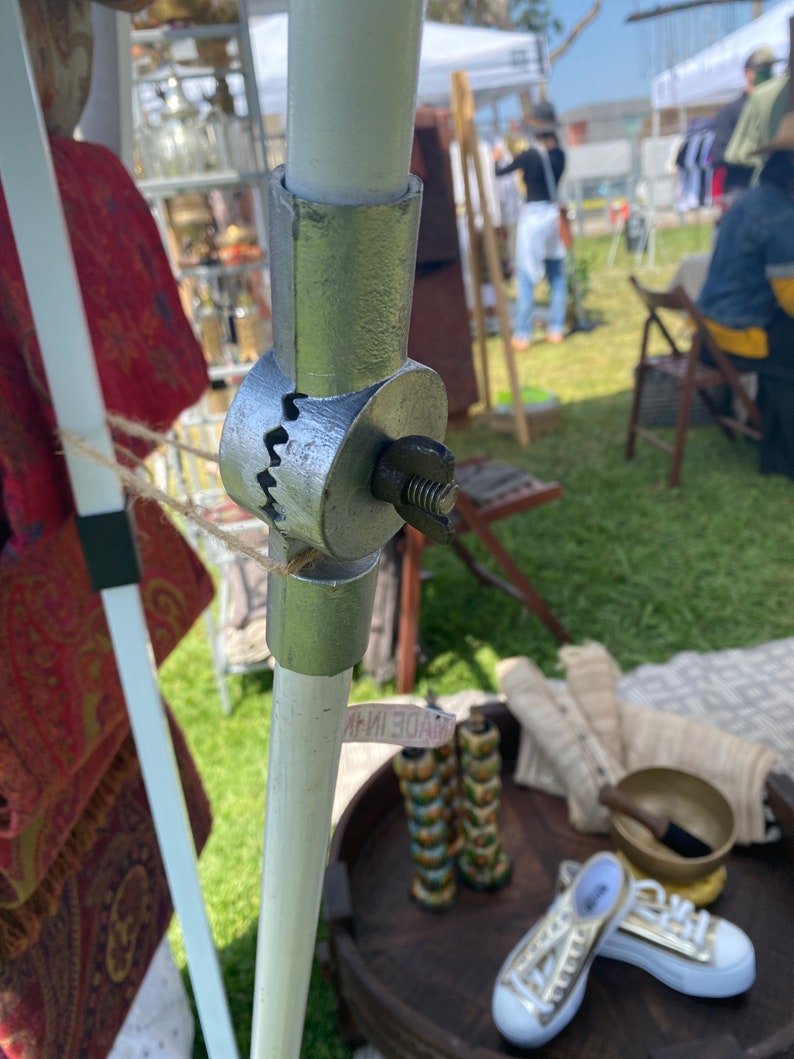 May include: A silver metal connector with a threaded screw, connecting two white poles. The connector has a serrated edge and is labeled "MADE IN CHINA".