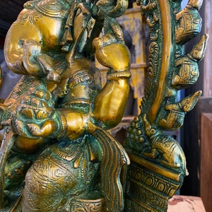 May include: A gold-toned brass statue of Ganesha, the Hindu god of wisdom and prosperity, sitting on a throne with intricate details. The statue is adorned with ornate carvings and a green patina.