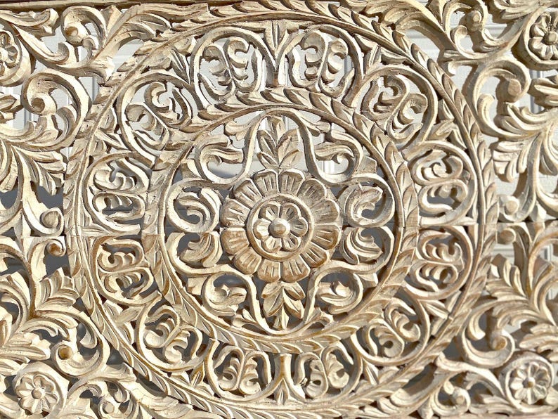 May include: Intricately carved wooden wall decor with a whitewashed finish. The design features a central floral motif surrounded by swirling patterns.