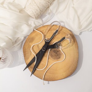 Può includere: Forbici nere con manici in plastica trasparente su una fetta di legno con una palla di spago naturale.