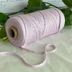 Peut inclure: Une bobine de cordon en coton de couleur lavande. Le cordon est enroulé serré autour d'un tube en carton. Un morceau de cordon pend de la bobine.