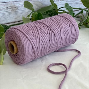 May include: A roll of lavender coloured cotton cord, with a length of cord extending from the roll.