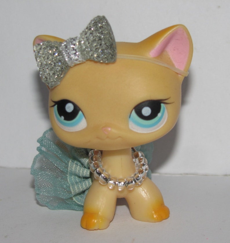 Puede incluir: Un peque&ntilde;o juguete de gato de color beige con un lazo de purpurina plateado, una falda de tul azul claro y un collar de cuentas plateadas.