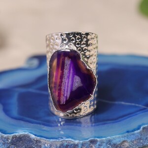 May include: A silver ring with a textured band and a large, irregular-shaped purple agate stone. The agate features bands of purple, pink, and white. The text "Exact Rings Same As Photo" is visible.