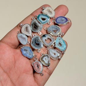 May include: A collection of small, irregular agate geode connectors featuring crystalline centers in various colors including blue, purple, white, and grey. Each stone is encased in a metallic silver-toned border with two small loops.