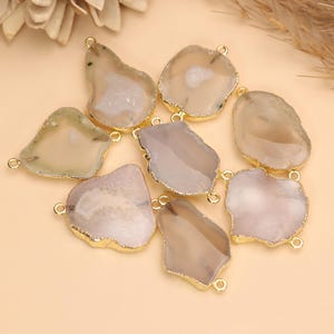 May include: A collection of irregular, translucent agate slices in shades of beige, cream, and soft gray. Each stone features a metallic gold-toned electroplated edge and includes two small circular jump rings attached to opposite sides for linking.