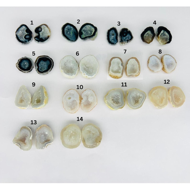 May include: Assortment of 14 pairs of natural geode halves, each with unique crystal formations and colors. The geodes range in size and shape, with some featuring black, white, and gray hues.