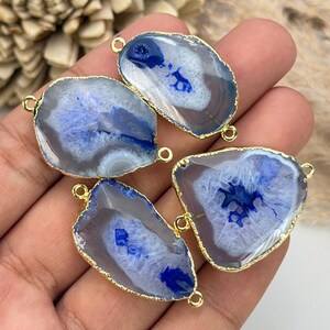 May include: Four irregular, translucent agate slices with vibrant blue centers and greyish-white outer edges. Each stone is encased in a thin, polished gold-tone metal rim and features two small gold-tone metal loops on opposite sides for attachment.