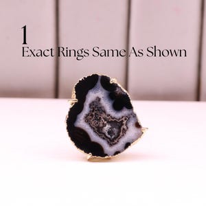 May include: A unique ring featuring a polished agate stone with black, white, and gray patterns, set in a gold-colored metal frame. The ring's irregular shape and natural stone design create a striking accessory. Text on the image reads: "Exact Rings Same As Shown."