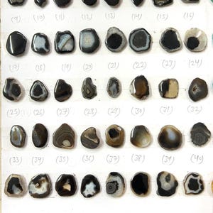 Puede incluir: Una colección de 40 rodajas de ágata negras y marrones, cada una con patrones y formas únicas. Los tamaños varían de 20-25. Las rodajas de ágata se muestran sobre una superficie blanca. El texto de la imagen dice "SIZE- 20-25 color- Black-Brown Agate Slice".