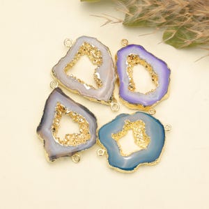 May include: Four irregular agate slice connectors with gold-plated edges. Each piece features a central hollow opening lined with sparkling gold druzy crystals. The slices are colored in shades of light gray, purple, dark gray, and blue.