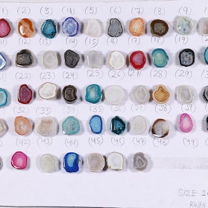 Könnte beinhalten: Eine Präsentation von 50 Achat-Scheiben, jede mit einem einzigartigen Muster und einer einzigartigen Farbe, angeordnet in Reihen auf einer weißen Oberfläche. Die Achat-Scheiben sind etwa 20 mm groß. Der Text "SIZE 20 MM Rings-Stone" ist unten im Bild gedruckt.