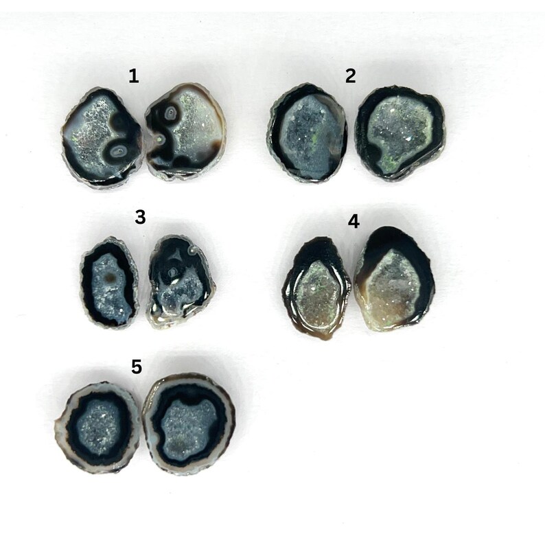 May include: Five pairs of agate slices with black edges. Each slice is unique and has a different pattern of white and gray crystals. The slices are numbered 1 through 5.